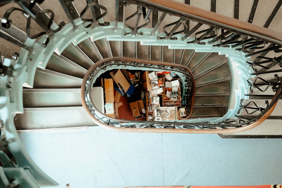 A top-down view of a metal staircase inside a property, showing ten textured, non-slip steps made of grey metal with a diamond pattern for safety. The staircase has dark grey metal railings on both si
